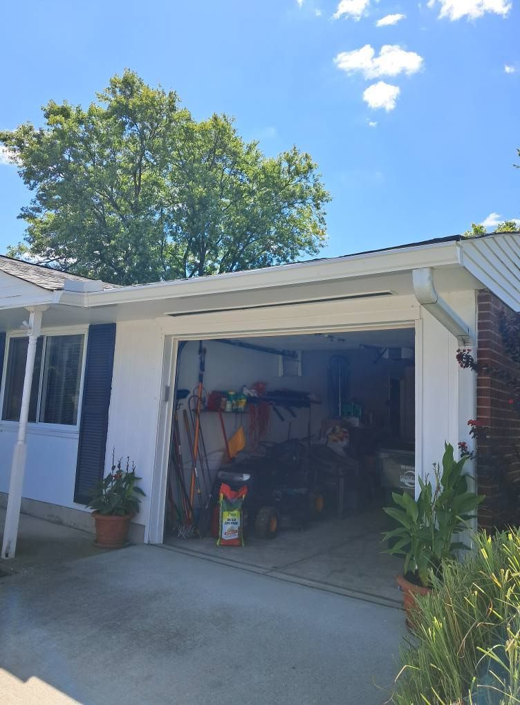 Garage with open door, various tools inside, white exterior, blue sky with tree in background. Garage with open door, various tools inside, white exterior, blue sky with tree in background.