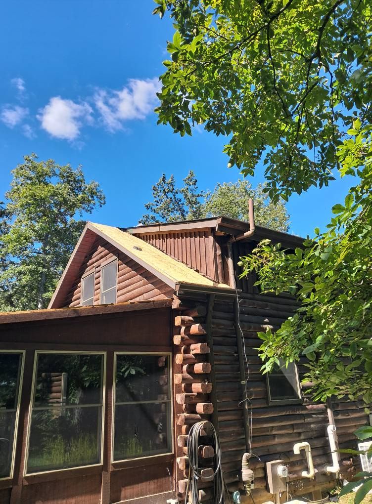 Log cabin exterior with trees under a blue sky. Wooden walls, windows, and a screened porch.