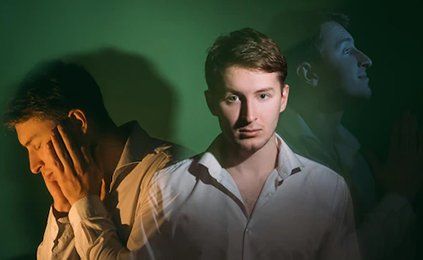 A man in a white shirt is standing in front of a green wall.