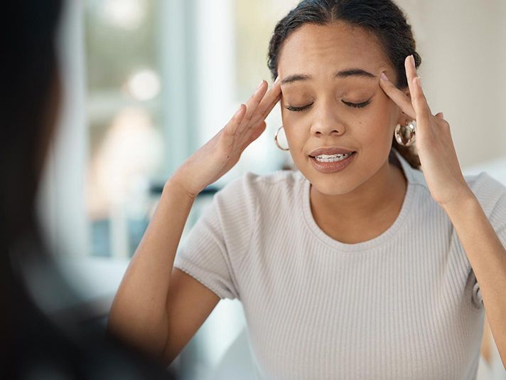 A woman is holding her head in pain while looking at herself in the mirror.