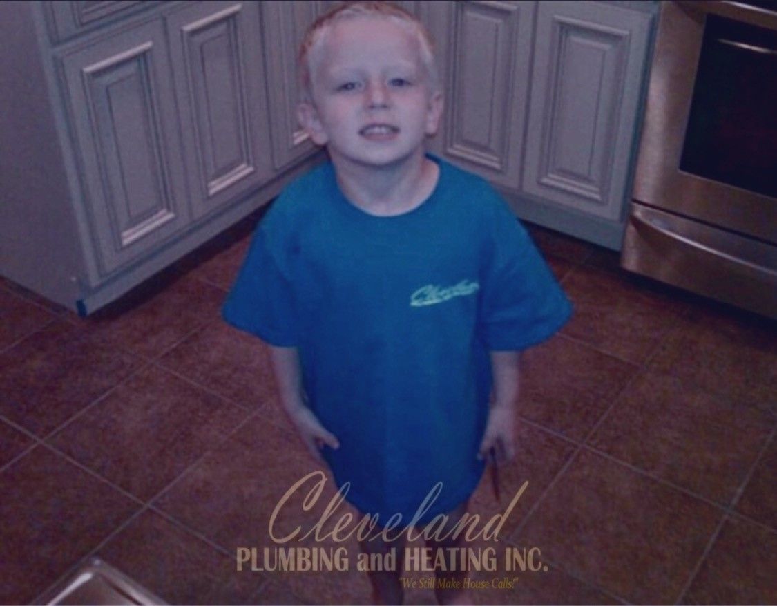 Young boy wearing a blue shirt, standing in a kitchen. Cleveland Plumbing and Heating Inc. logo is at the bottom.