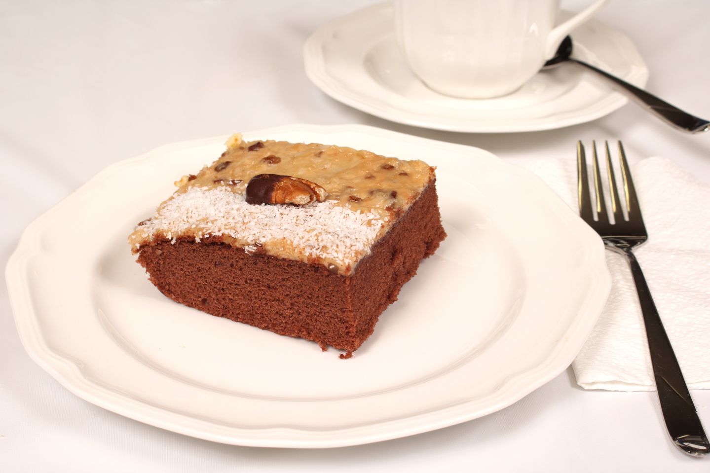 Chocolate cake slice on a white plate, with a fork and teacup.