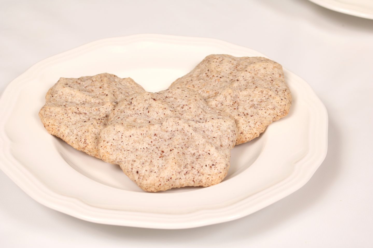 Three light-brown, speckled cookies on a white plate.