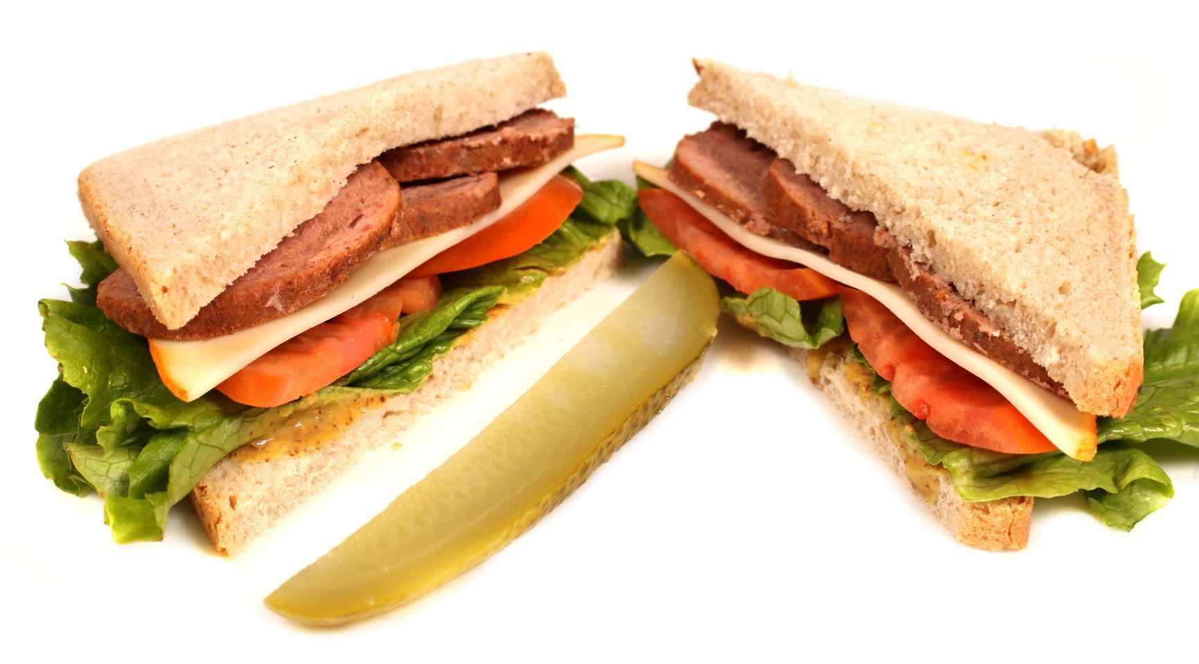 Two cut sandwiches with sausage, tomato, cheese, lettuce and pickle.