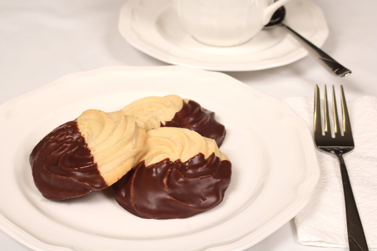 Cookies dipped in chocolate on a white plate, with teacup and fork.