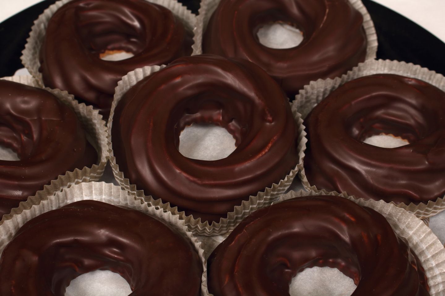 Chocolate-covered donuts in paper liners, close-up, piled in a circle.