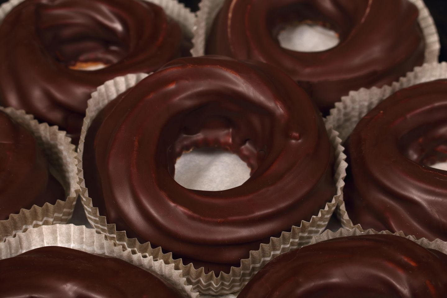 Chocolate-covered donuts, round with open centers, in paper liners.
