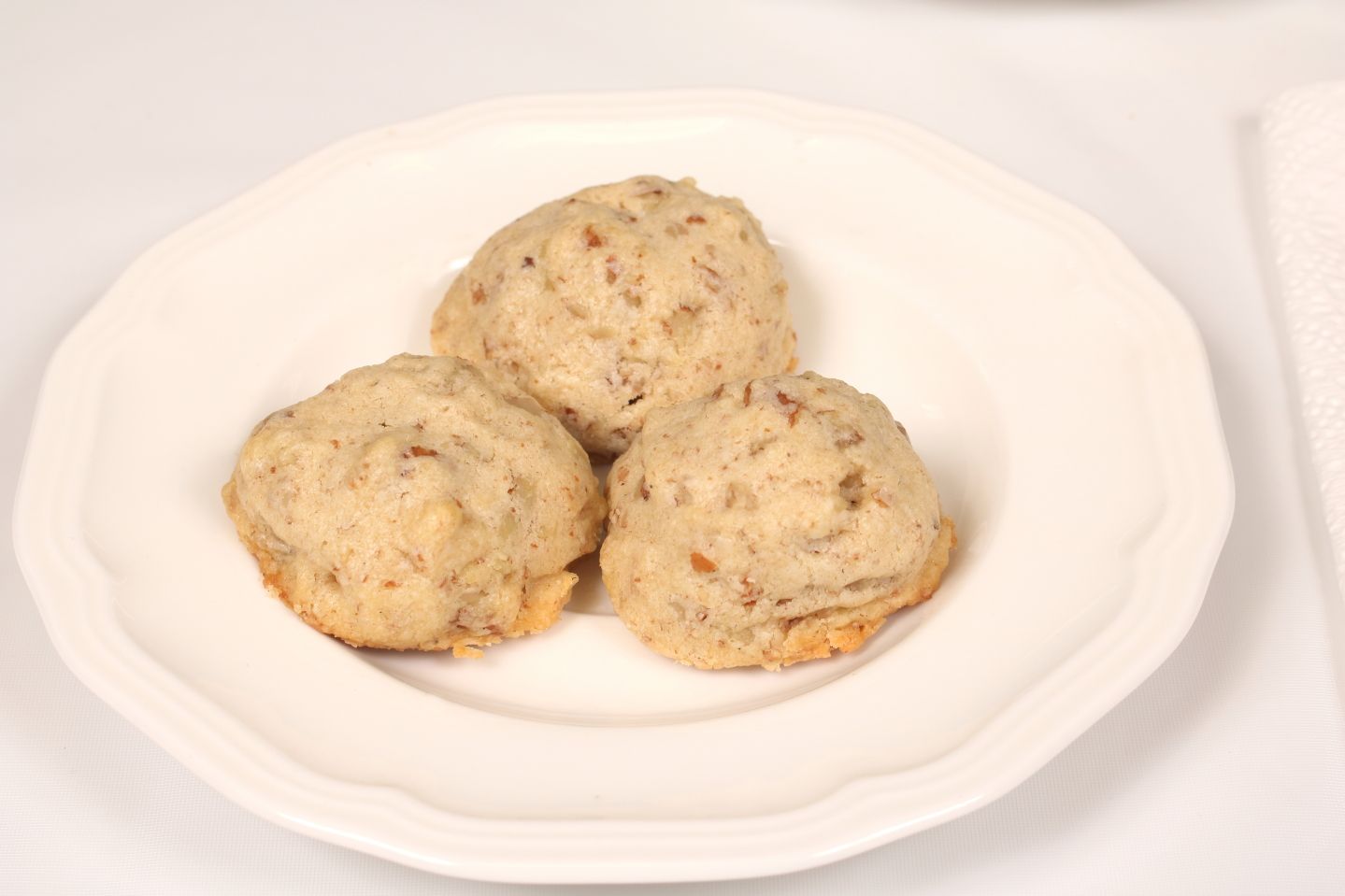Three round cookies with nuts on a white plate.
