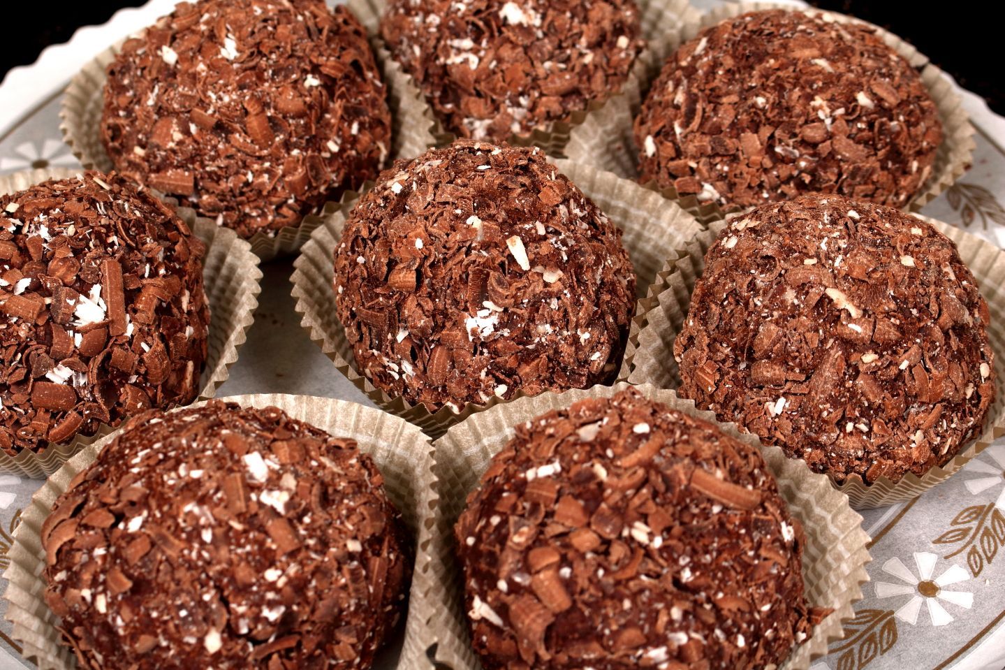 Chocolate truffles in paper cups, coated with chocolate shavings, arranged on a plate.