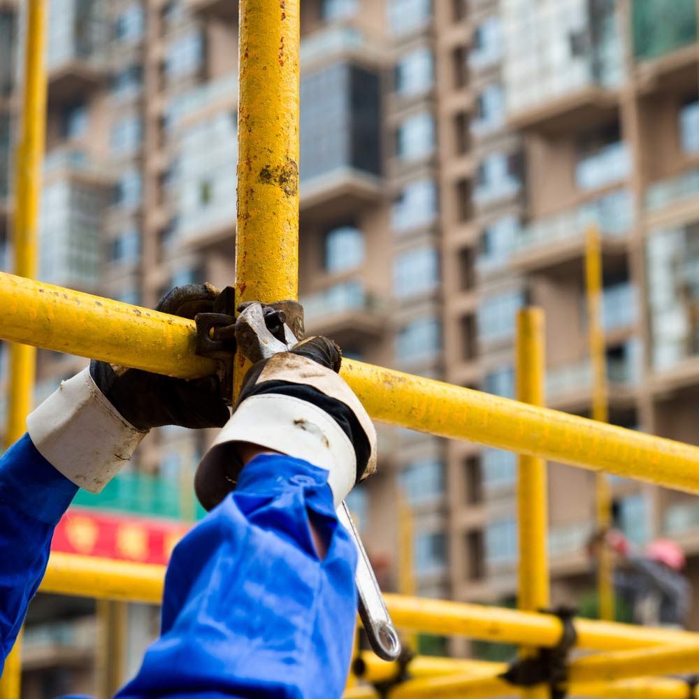 A Person Wearing Blue Gloves Is Working On A Yellow Scaffolding — Triple S Scaffolding In Forster, NSW