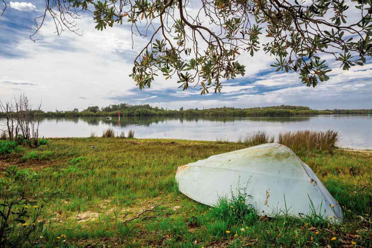 A White Boat Is Sitting On The Shore Of A Lake — Triple S Scaffolding In Taree, NSW