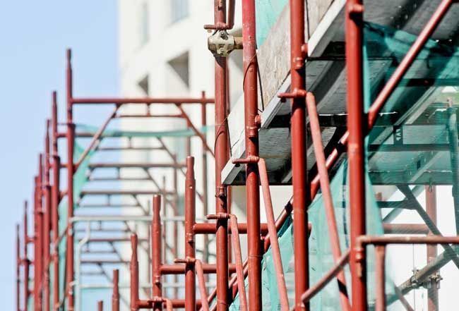 A Row Of Red Scaffolding Is Lined Up In Front Of A Building Under Construction — Triple S Scaffolding In South West Rocks, NSW