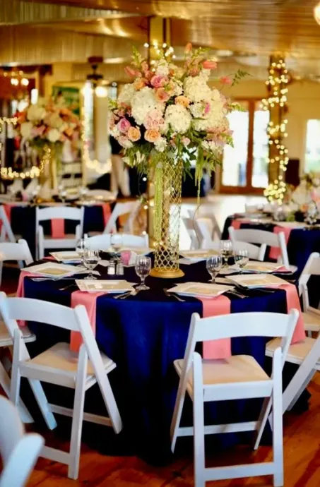 Navy and pink wedding reception tables with floral centerpieces and white chairs.