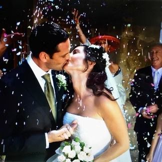 Wedding couple kissing, showered with confetti. Outdoors; man in suit, woman in strapless white dress.