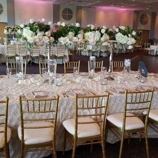 Elegant banquet table set with white floral arrangements and gold chairs.