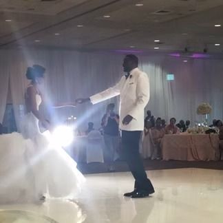 Bride and groom dance at a wedding reception on a shiny dance floor; the bride wears white, the groom a white jacket.