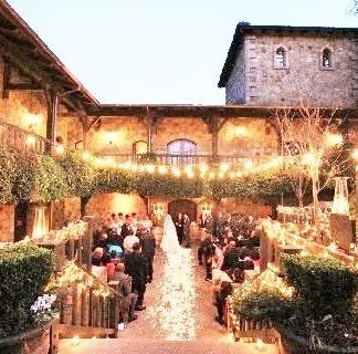 Wedding ceremony in a stone courtyard with guests, a bride walking an aisle of petals, and a stone tower.