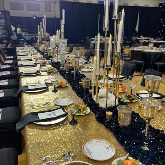 Long banquet table with gold tablecloth, black runner, candles, and place settings.