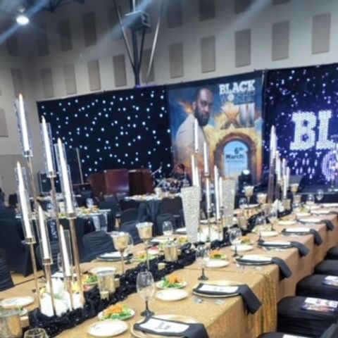 Formal dinner table setting with candles, gold tablecloth, and event banner.
