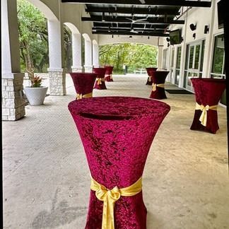 Burgundy velvet cocktail tables with gold bows on a covered patio.