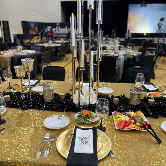 Formal event table setting with gold and black decor. Candles and food on a golden tablecloth.