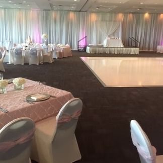 Wedding reception hall with pink and white decor, dance floor, and stage.