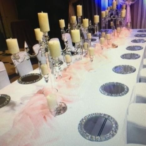 Long table set for a formal event with white linens, candelabras, candles, and pink chiffon.