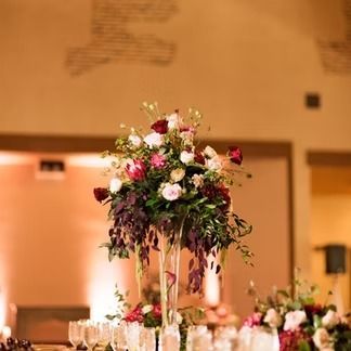 Elegant floral centerpiece in tall glass vase, with burgundy and white blooms, in a warm-lit room.