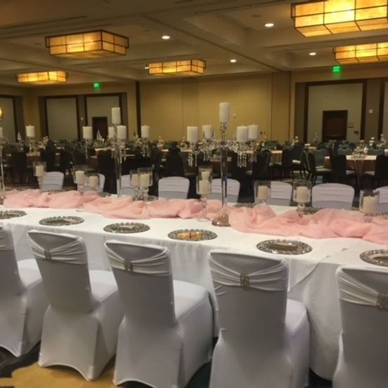 Formal event space with white-covered tables, chairs, pink runners, and candelabras.