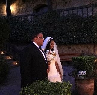 Father and bride walking outside at wedding; bride wears white dress and veil, father wears tuxedo.