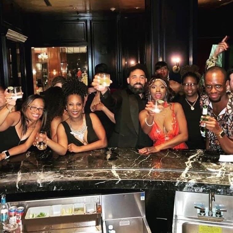 Group of people at a bar, smiling, raising glasses for a toast. Dark setting, marble counter.
