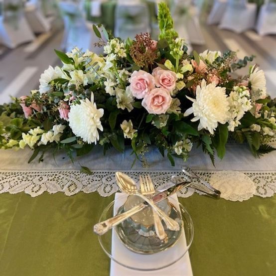 Wedding table setting: centerpiece of white and pink flowers, silverware, and green tablecloth.