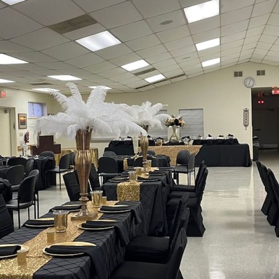 Black and gold tables set for a formal event with feather centerpieces in a large room.