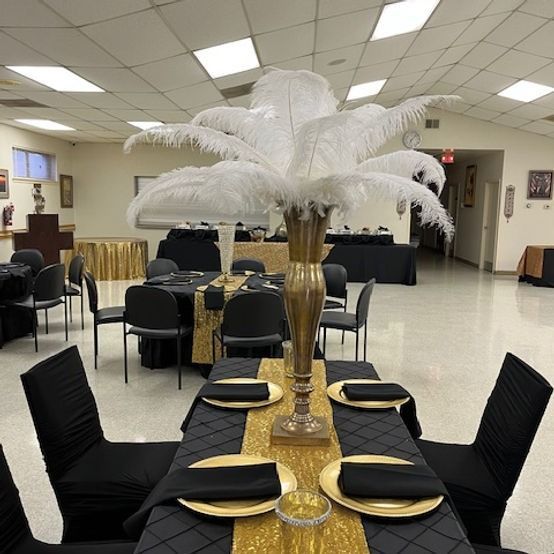 Elegant event setup with black and gold tables, feather centerpiece in a large room.