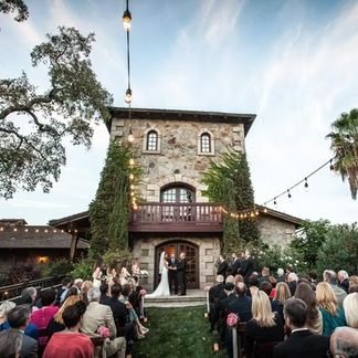 Wedding ceremony at stone tower. Bride and groom stand at altar, guests seated on lawn.
