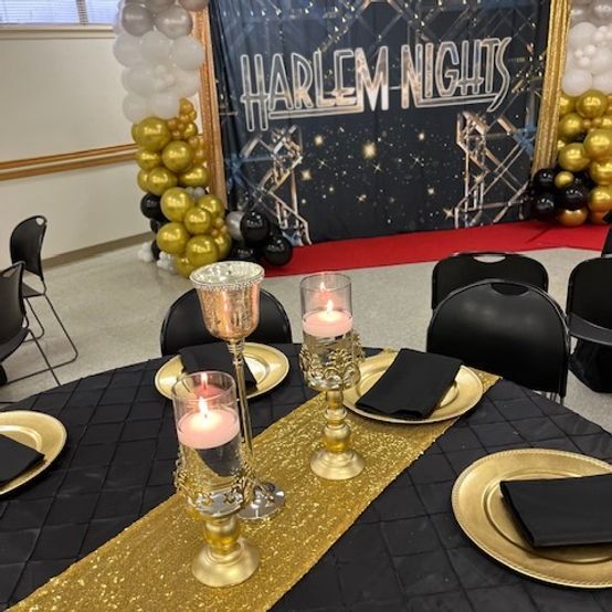 Harlem Nights party scene with black, gold decor. Tables set for guests. Balloons and backdrop.