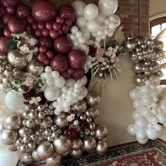 Balloon wall with maroon, white, and silver balloons and floral accents, set against a brick wall.