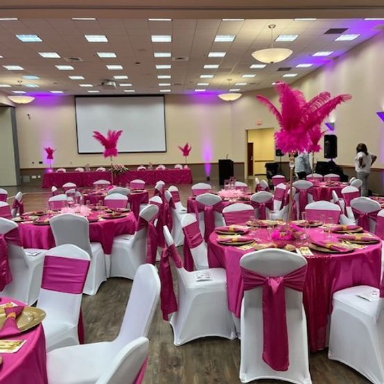Pink and white decorated event hall with tables, chairs, and feather centerpieces, ready for a celebration.