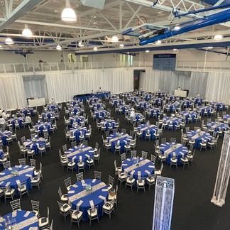 Large room set up with many round tables covered in blue cloths for an event.