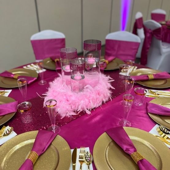 Formal table setting with gold chargers, pink linens, and a feather centerpiece.