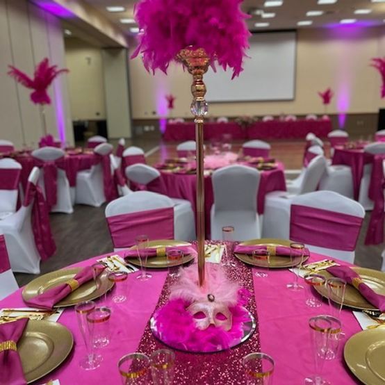 A ballroom set for a party with hot pink decor, gold accents, and feathered centerpieces.