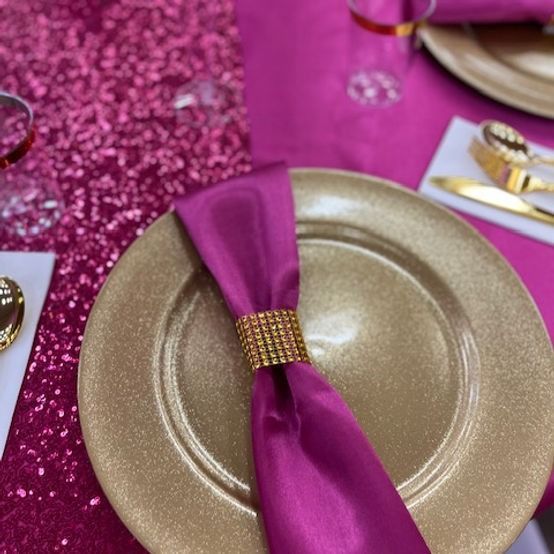 Gold charger plate with magenta napkin and gold ring, on a sequined table setting.
