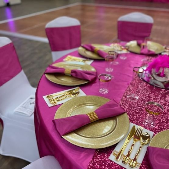 A formal table setting with gold chargers, fuchsia napkins, and pink table cloth.