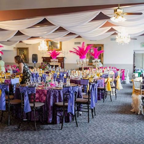 Elegant banquet hall, tables set with purple, yellow, and gold decorations. Pink feather centerpieces.