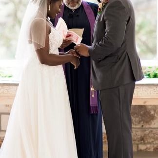 Bride and groom exchange rings during wedding ceremony, officiated by priest.