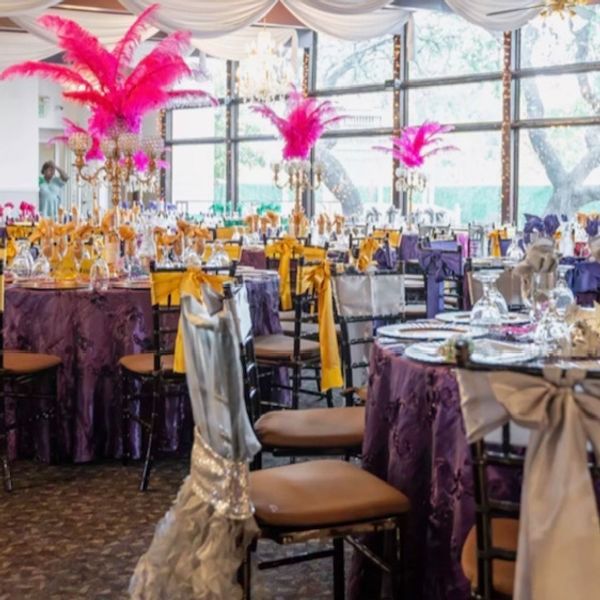 Banquet hall with tables draped in purple and gold, adorned with pink feather centerpieces.