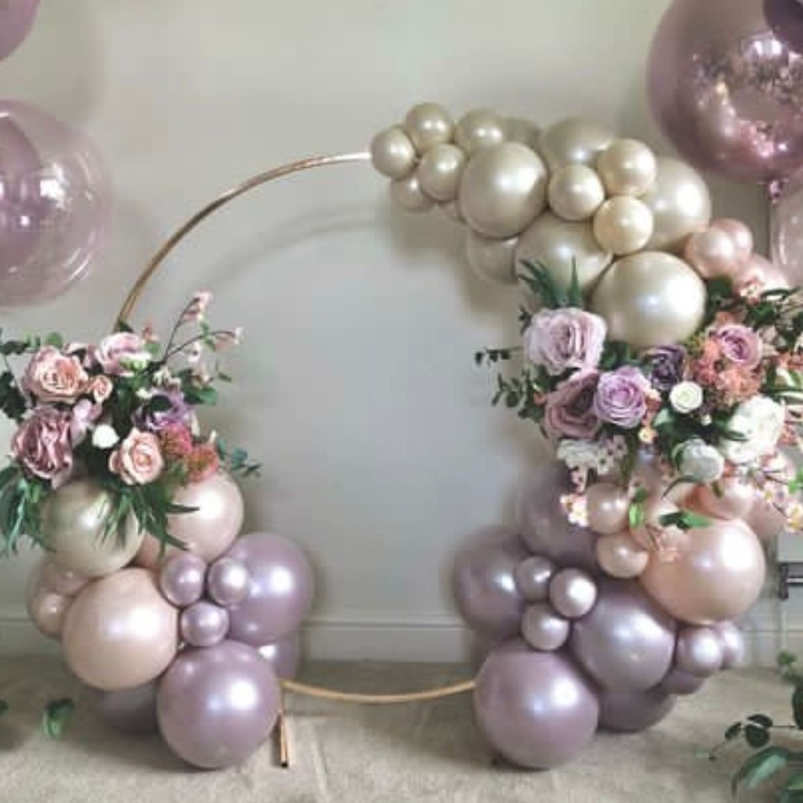 Gold hoop decorated with balloons and flowers in shades of pink and purple.