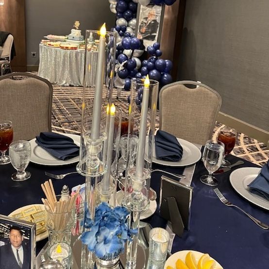 Formal table setting with candles, blue napkins, and a decorated buffet in the background.