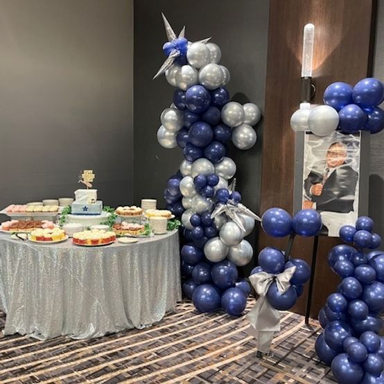 Party decorations with balloons, table with food, and a photo display in a room.