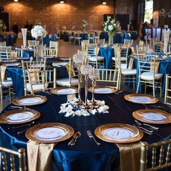 Round tables set for a formal event with navy blue tablecloths, gold chargers, and floral centerpieces.